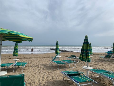 Grüne Liegestühle mit Schirmen auf dem Sand direkt am Meer in Jesolo. 