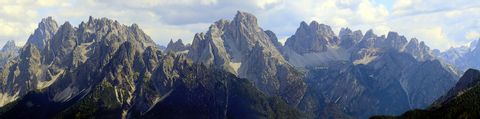 Über ein Panoramabild sind die Dolomiten in verschiedenen grautönen zu sehen Am Himmel hat es einige weisse und graue Quellwolken.