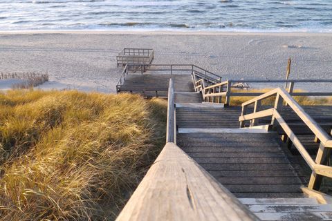 Eine Holztreppe führt hinab auf einen Sandstrand an der Nordsee.