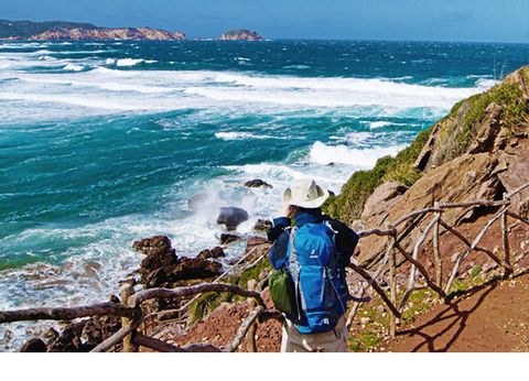 Ein Wanderer sitzt auf einem Felsenabschnit am Küstenweg auf Menorca.