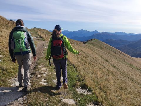 Zwei Wanderinnen laufen auf einem Naturweg zwischen den Bergen.