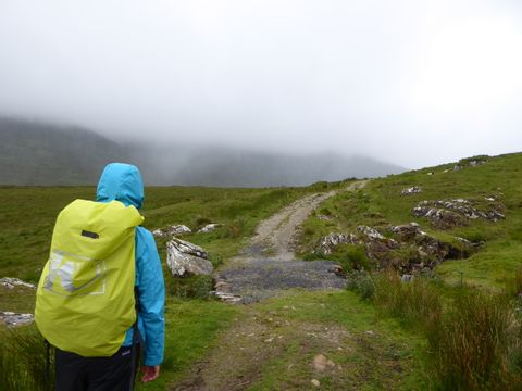 Ein Wanderer umgeben von grüner Wiese auf dem West Highland Way in Irland bei Regen.