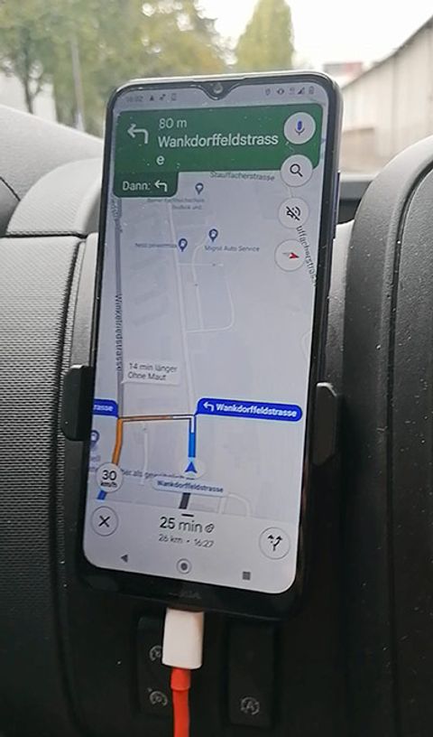 Ein Handy das an der Konsole eines Autos befestigt ist und Google Maps zeigt den richtigen Weg.
