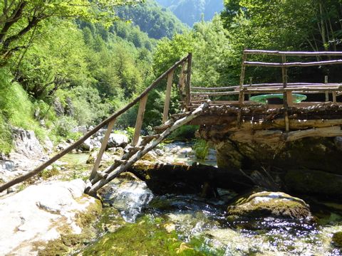 Eine alte Brücke aus Holzstämmen, führt über einen Bach der durch den Wald läuft.