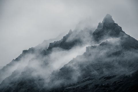 Ein schwarzer Berg im sehr dichten Nebel füllt das ganze Bild.