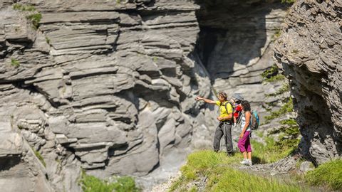Ein Wandererpärchen vor einer riesegen Felswand die aussieht, als wäre es ein Stapel Steinplatten.