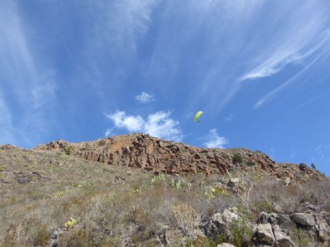 Zwischen der Bergspitze und dem strahlend blauen Himmel ist ein Paraglider mit gelbem Gleitschirm am schweben.