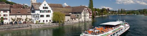 Ein weisses Schiff fährt mit Touristen auf dem Bodensee. Af der linken Seite stehen die Häuser von Stein am Rhein.