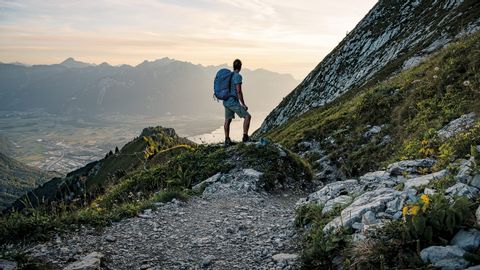 Ein einzelner Wanderer mit Ruckasack schaut vom Berg ins Tal hinunter .