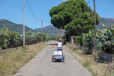 Eine Velofahrerin fährt mit Kinderwagen auf einer schmalen Strasse auf Sardinien.