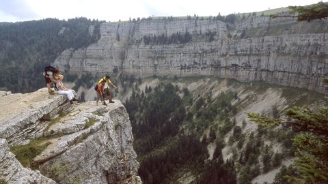 Four hikers take a break, while one stands at the front of the precipice and shows another person the gorge.