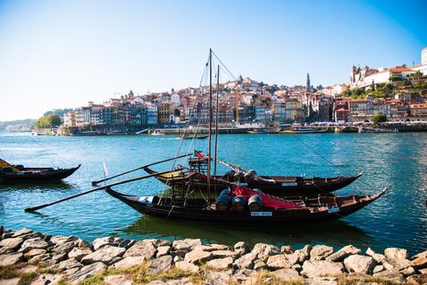 Zwei mit Fässern beladene Segelschiffe, sind nebeneinader am Steg befestigt. Am gegenüberliegenden Ufer die Stadt Douro.