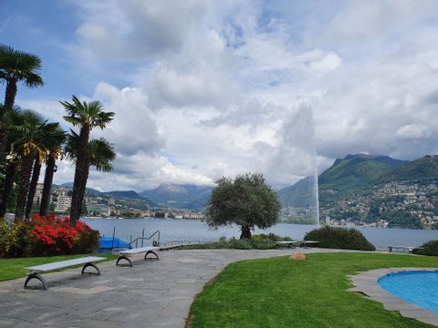 Von einem Platz mit Springbrunnen aus sieht man auf die Fontäne im See vor Lugano. 