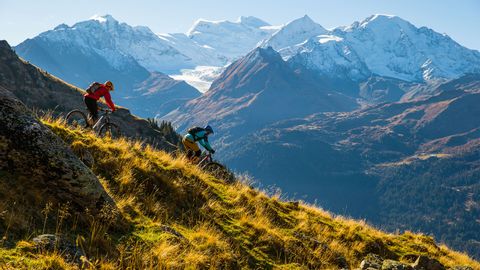 Two trail runners descend the mountain on a natural path. A magical mountain landscape in the background. Some of the mountain peaks are covered in snow.