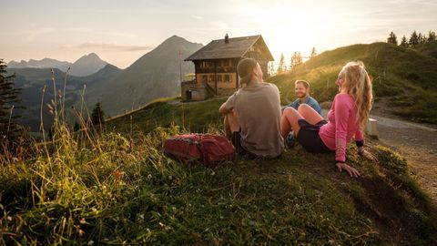 Drei Personen entspannen auf einer kleinen Anhöhung mit Ausblick ins Tal in der Region Fribourg.