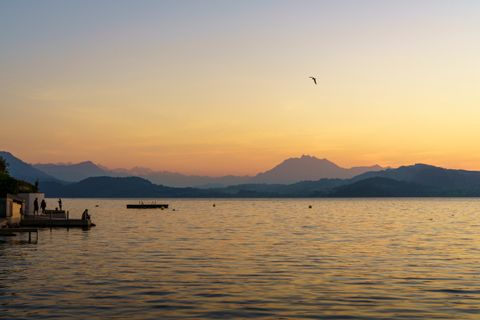 Von Zug sieht man auf den See mit den dahinterliegenden Bergen bei Sonnenuntergang. 