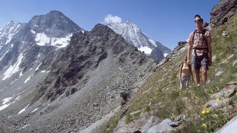 Deux randonneurs sur le sentier des cols alpins en Valais, avec vue sur le paysage de montagnes rocailleuses en arrière-plan.