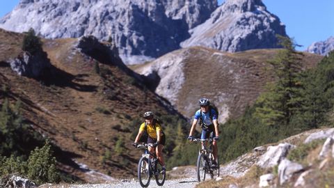 Two mountain bikers on a rocky path. The mighty Grisons mountains in the background.