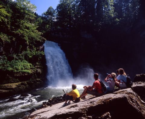 Familie, welche auf einem Stein sitzt und den Wasserfall Saut du Doubs bestaunt. Aktivferien mit Eurotrek.