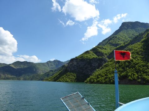 Die Spitze eines Bootes mit der Albanischen Flagge. Die fahrt führt an den wunderschönen Bergen vorbei.