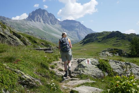 Wanderin läuft über einen Steinabschnitt über die Almwiese auf die Berge im Hintergrund zu.