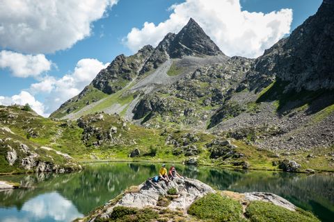 Zwei Trail Runner machen Pause an einem Bergsee in der Via Grischuna.