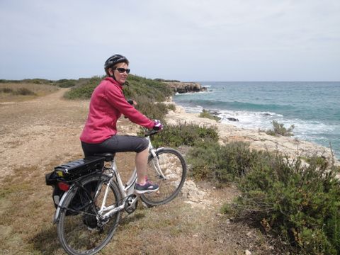 Velofahrerin steht an einer Klippe und betrachtet das Meer. Sizilien Südost. Veloferien mit Eurotrek. 