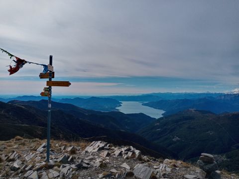 Ein Wegweiser vor einem wolkenbedeckten Bergpanorama. Sentiero Lago di Lugano. Wanderferien mit Eurotrek.