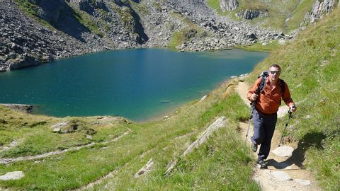 Wanderer auf einem Anstieg auf einen Berg mit kleinem See im Hintergrund