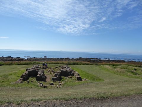 Ein Päärchen macht auf Steinruinen, an der Küste ein Päuschen und geniesst die Aussicht. Küstenwandern in Schottland. Wanderferien mit Eurotrek.