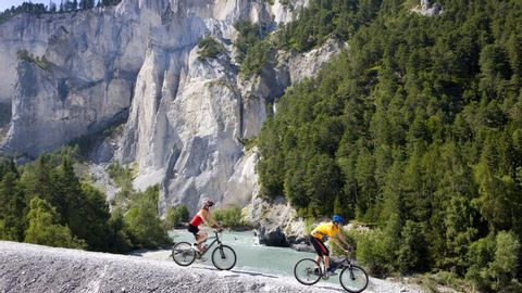 Zwei Mountainbiker auf der Naturstrasse vor der Felswand.