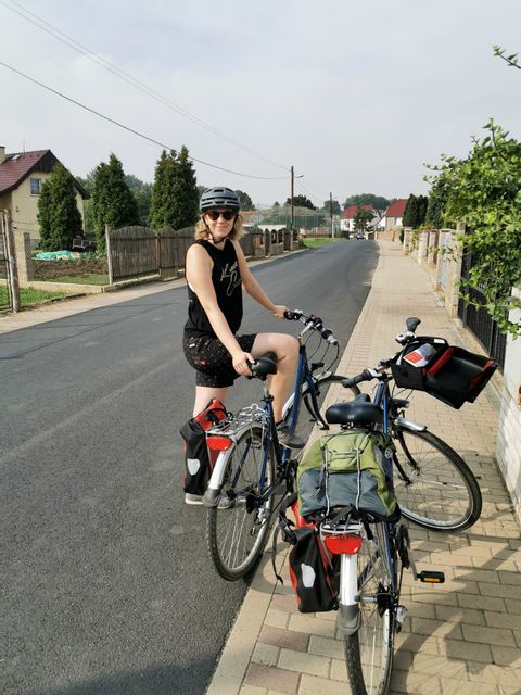 Eine Velofahrerin steht mit 2 Bikes auf dem Trotoir und lächelt in die Kamera.