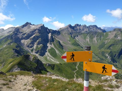 Ein Wanderwegweiser steht vor einer grünen Bergkulisse in Liechtenstein. 