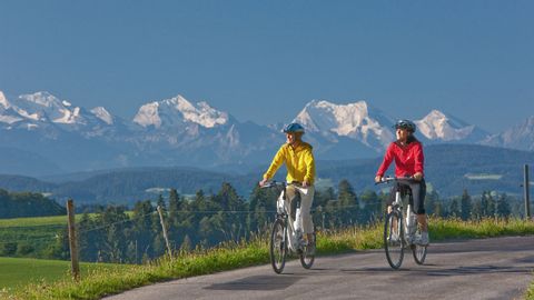 Zwei Radfahrer fahren durch Affoltern im Emmental mit Blick auf die Alpen.