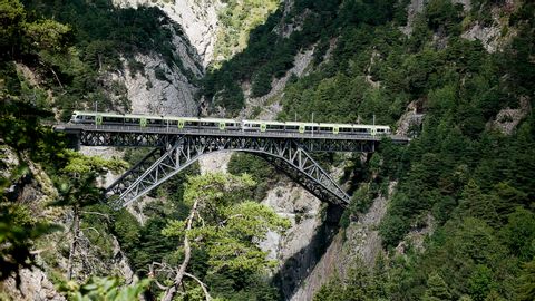 Hellgrün/weisser Zug fährt auf der Brücke über die Schlucht beim Lötschberg