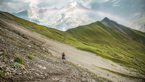 Ein Wanderer steht auf dem Alpschelegrat über Kandersteg. Über die Bergspitzen strahlt ein Regenbogen.