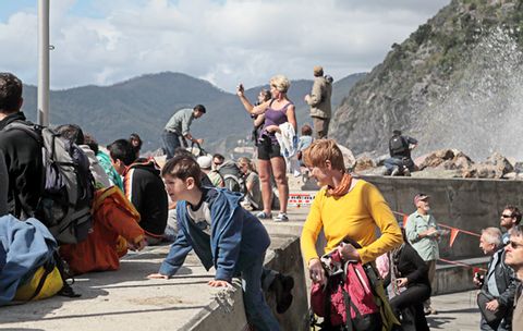 Sehr viele Touristen, darunter auch Kinder, sitzen am Ufer des Hafens von Vernazza.