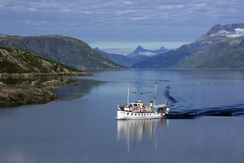 Ein Boot auf dem Bitihorn See in Norwegen fährt auf blauem Wasser durch die bergige Landschaft. 