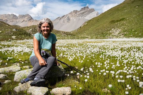 Eine Frau sitzt in einer Blumenwiese in den Bergen Graubündens.