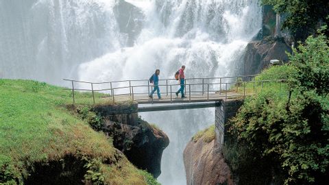 Deux personnes sur un pont et une grande chute d'eau en arrière-plan. Via Souvorov. Vacances de randonnée avec Eurotrek.