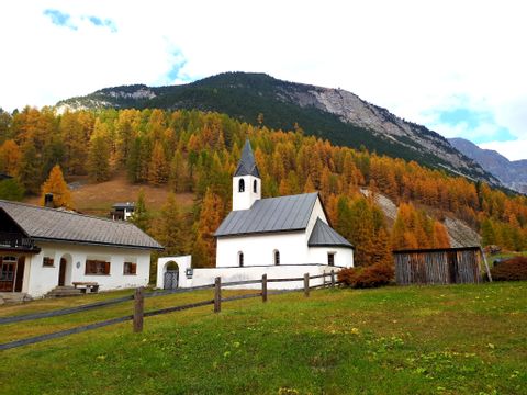 Eine kleine Kirche mit einem Haus daneben, am Fusse des Berges.