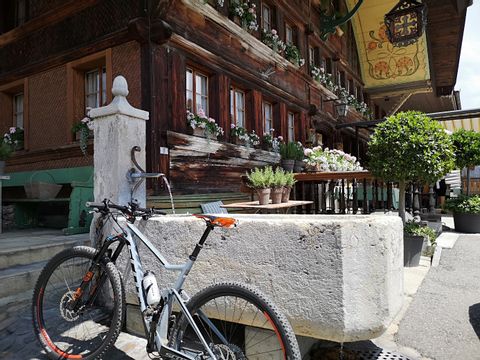 Ein Mountainbike angelehnt an einen steinernen Dorfbrunnen vor einem alten Haus.