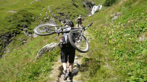 Personne forte qui porte le vélo sur ses épaules. Vélo alpin. Vacances à vélo avec Eurotrek.