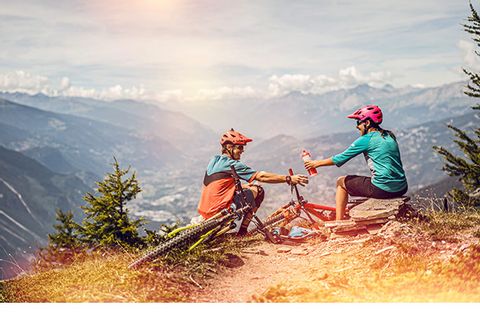 Zwei Mountainbiker machen Rast auf einem Rastplatz mit weitläufiger Aussicht auf Leukerbad im Kanton Wallis.