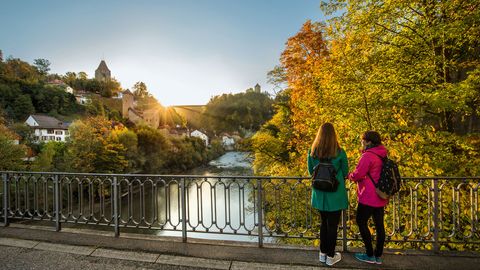 Des randonneuses se tiennent sur un pont et regardent les châteaux du Hühel en face d'elles.