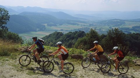 Quatre cyclistes roulent sur un chemin de terre dans le Jura avec un panorama en arrière-plan.