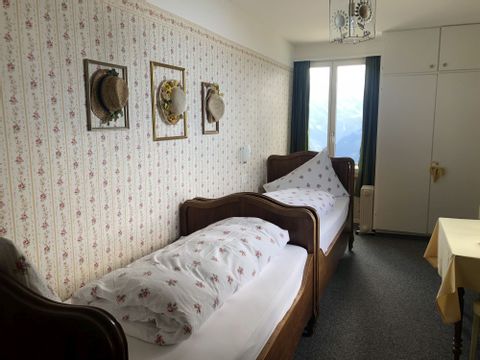 Zwei holzige Einzelbetten vor einer Blumentapete im Berghotel Schynige Platte mit Aussicht auf den Brienzersee. 