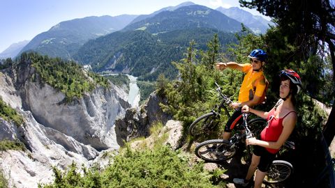 Zwei Mountainbiker stehen an einem Abgrund und blicken auf die Schlucht des Vorderrheins in Graubünden.