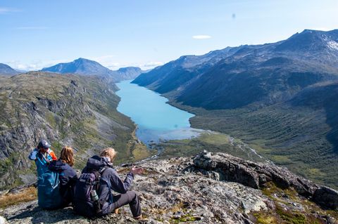 Drei Wanderer sitzen bei Gjendetunga in Norwegen und schauen auf den See, der unter ihnen liegt. 
