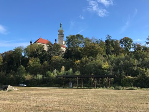 Hinter einem kleinen Wald und trockener Wiese, vesteckt sich eine Kirche links, und rechts ist noch ein Teil eines Turmes zu sehen.